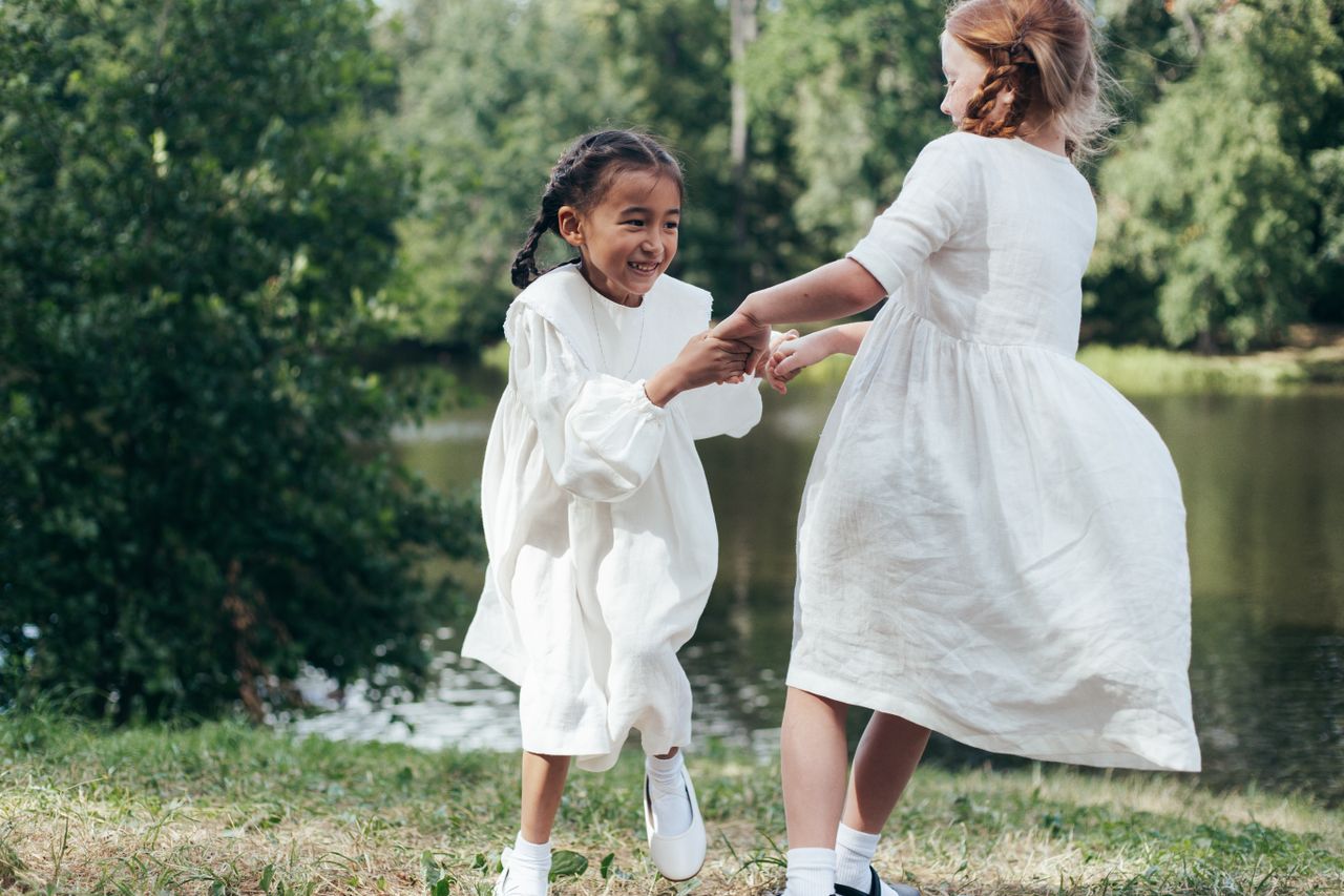Two girls joyfully dancing in a verdant park, surrounded by lush greenery.