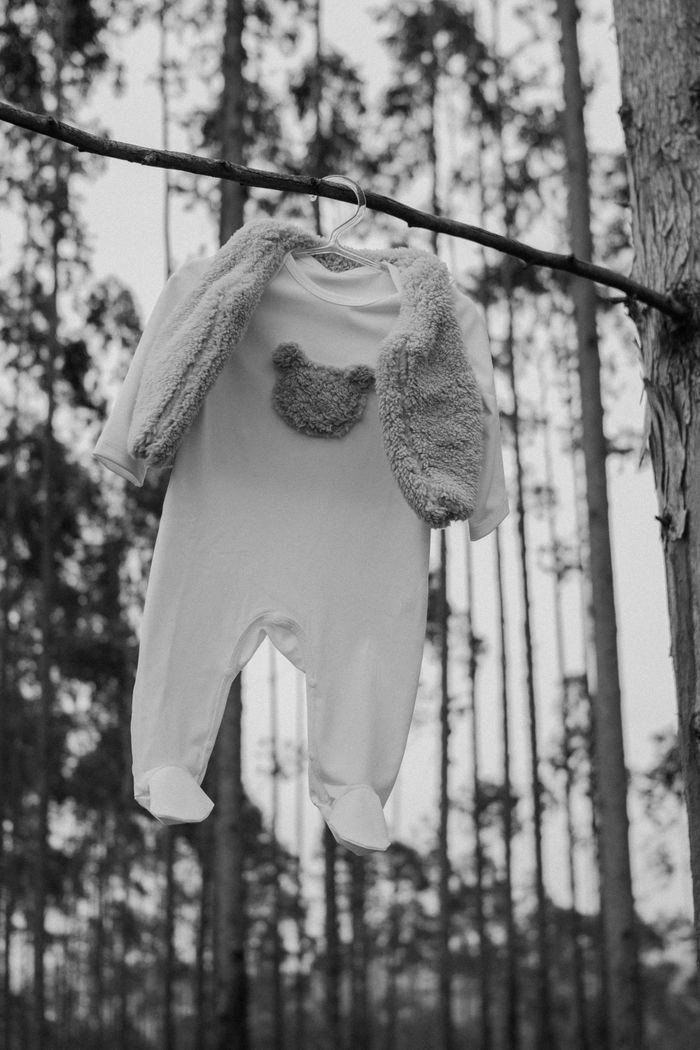 A monochrome baby outfit hung on a tree branch in a serene forest setting.