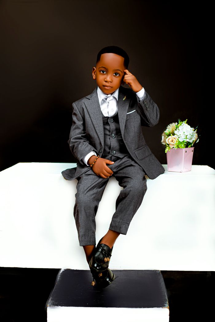 Young boy in gray suit with flowers in studio setting.